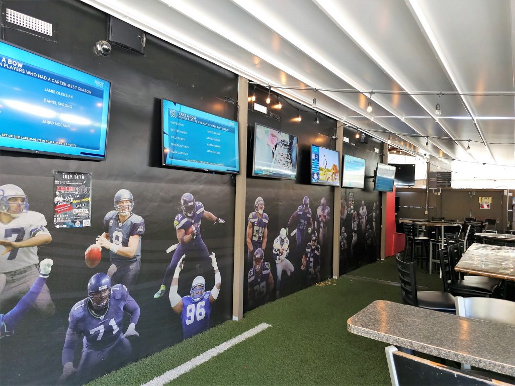 Inside Charlie's Bar with flat screens lining the wall, football player stickers underneath, astroturf ground and big long tables