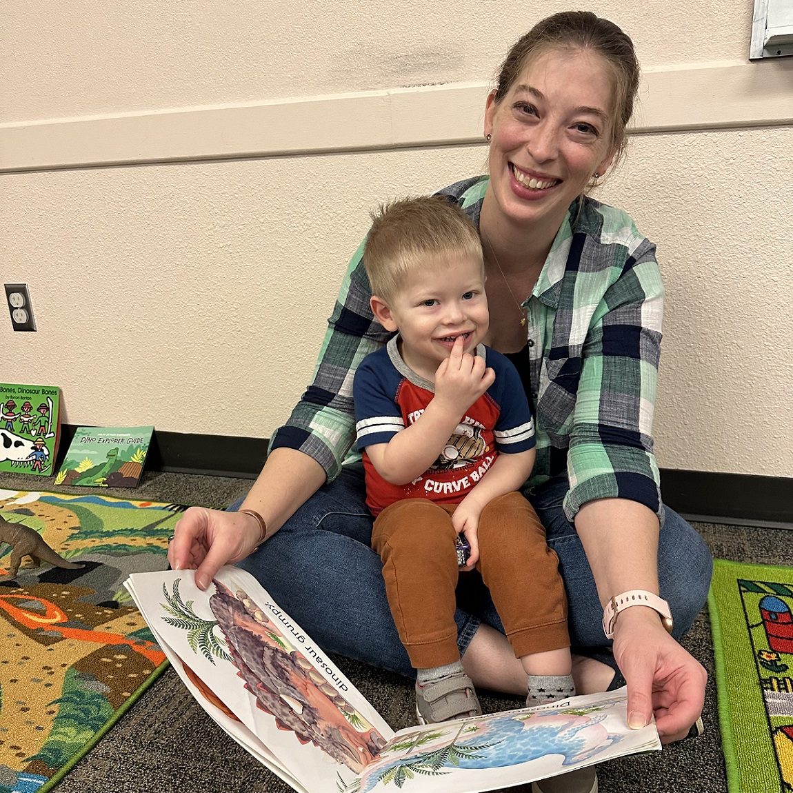 woman holding sitting on floor with a child on her lap showing him a book
