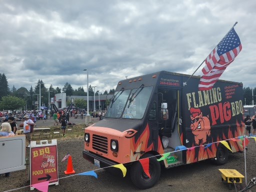 Flaming Pig BBQ truck sitting outside a high school building with lots of people and cars in the background