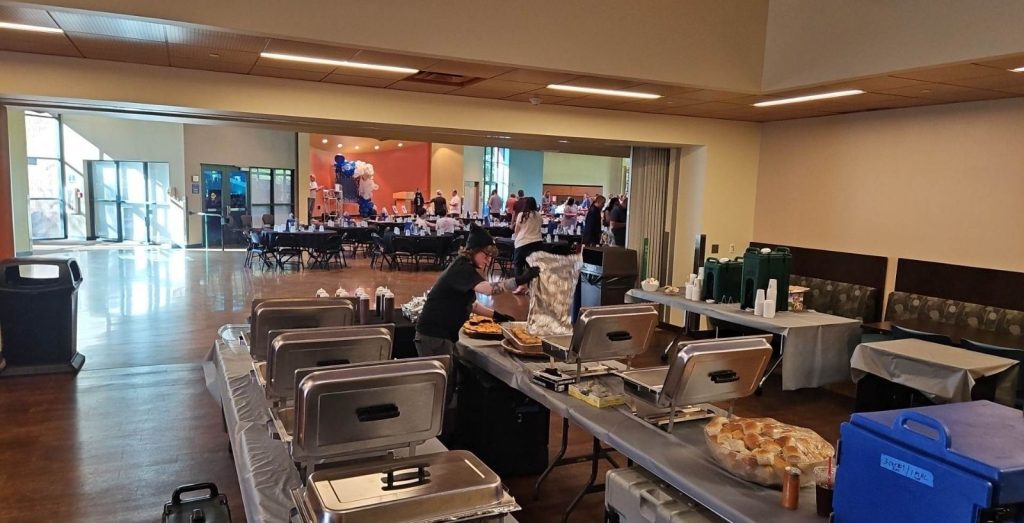 tables with black tablecloths and chairs inside a school building with a close up of metal catering pans