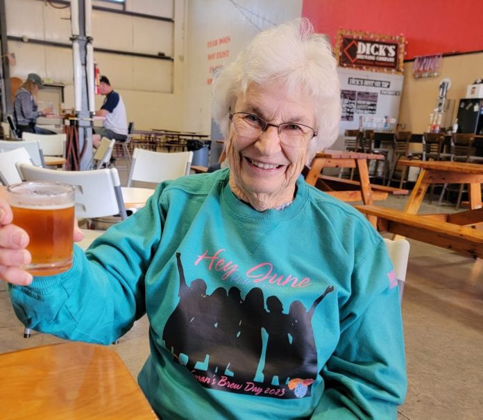 lady with white hair in a teal sweatshirt raising a glass of beer