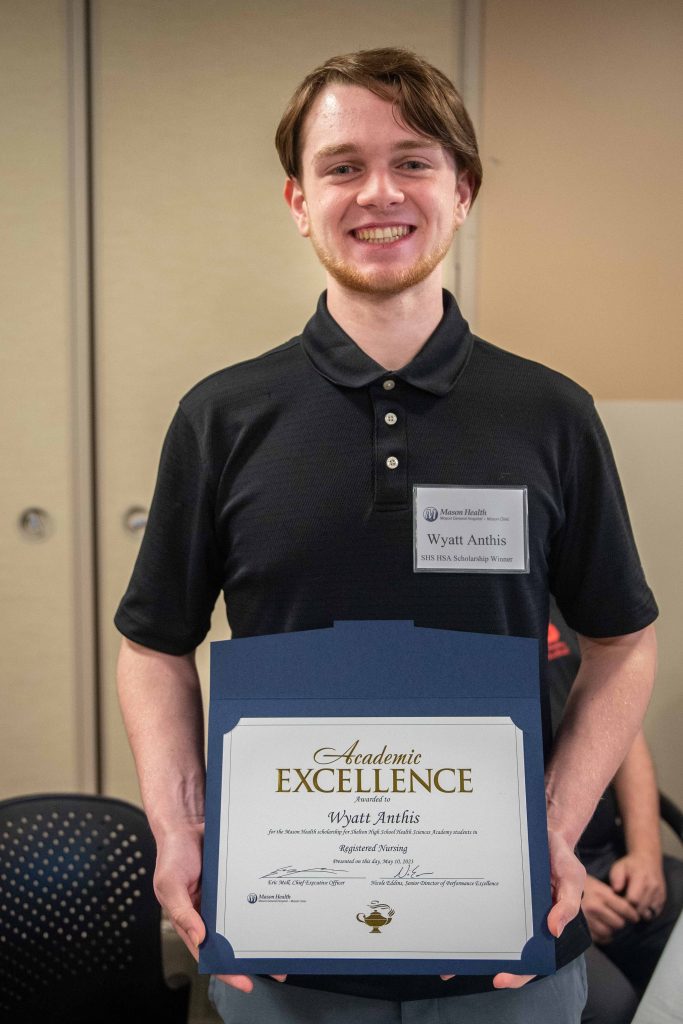 Wyatt Anthis standing holding his Academic Excellence certificate with blue and silver balloons behind him