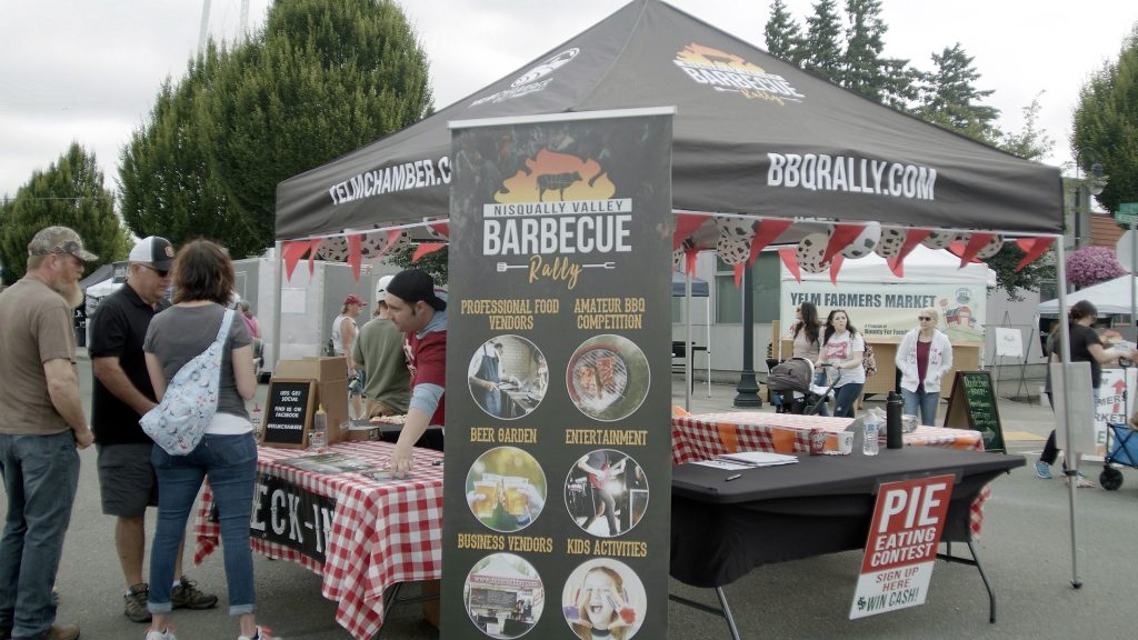 Nisqually Valley Barbecue Rally pop up tent with lots of signage and a few people milling about