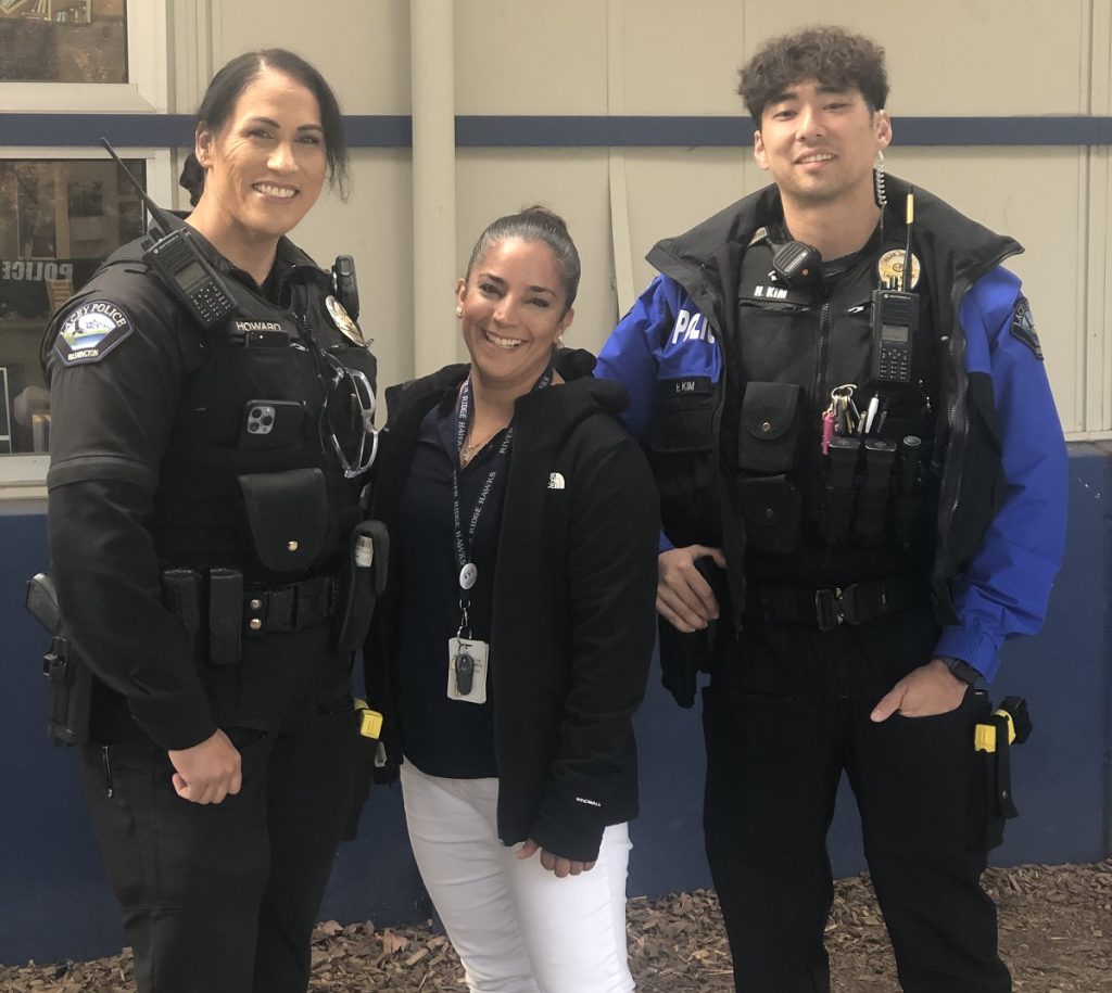 a woman stands between to security guards at a school. They are all smiling at the camera