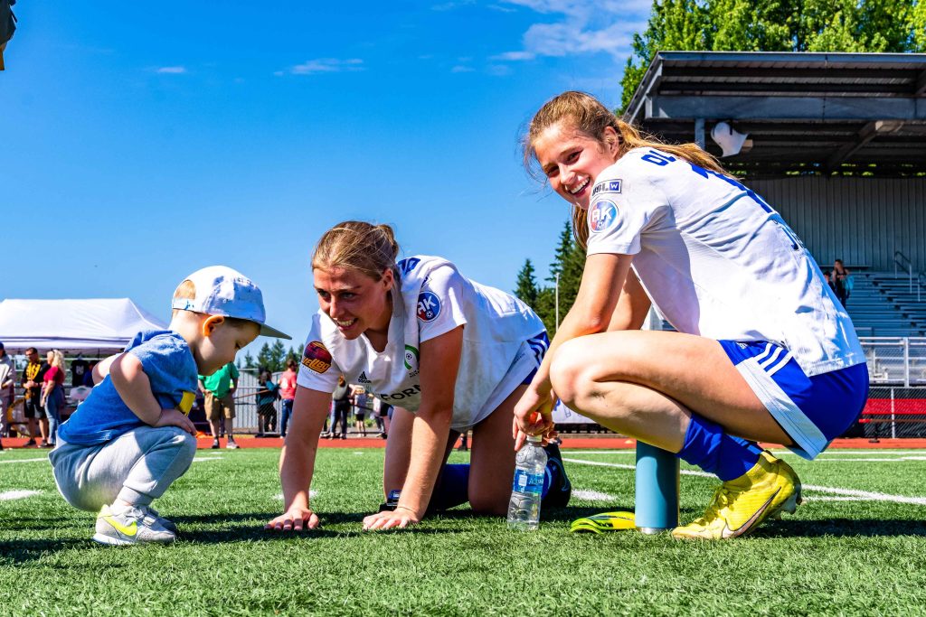 two female soccer players crouched down on the grass with a boy