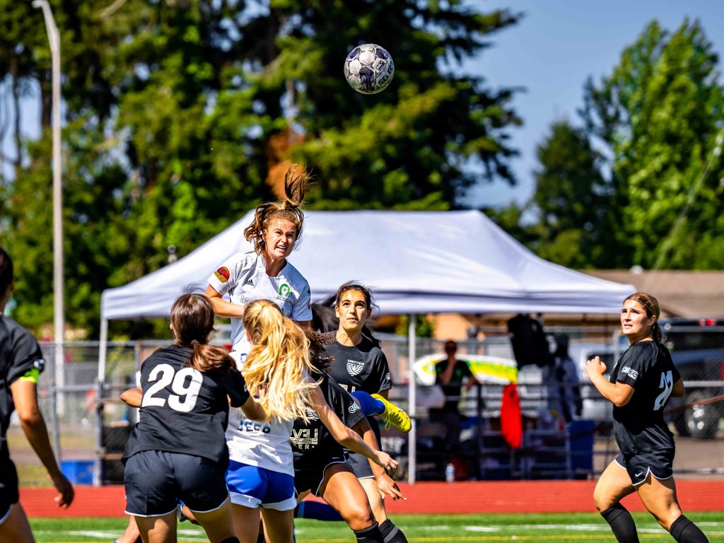 women soccer player leaps out of a group and head butts ball