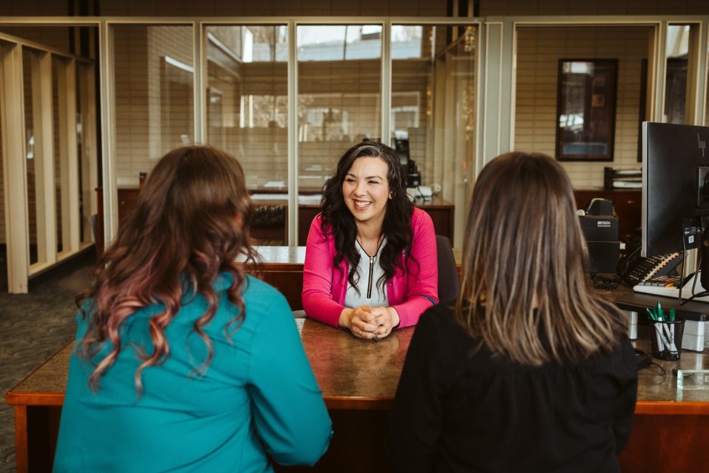 three women sitting at a table, one is facing the other two, those backs are to the camera