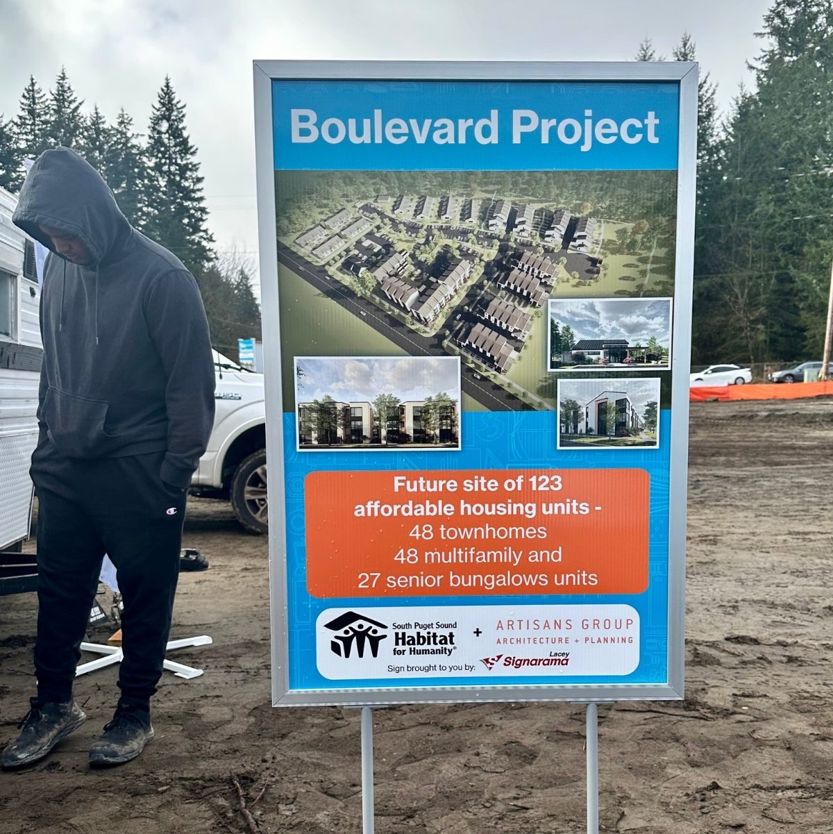 a person standing by a sign that says, 'Boulevard Project: Future site of 123 affordable housing units - 48 townhomes, 48 multifamily and 27 senior bungalows'