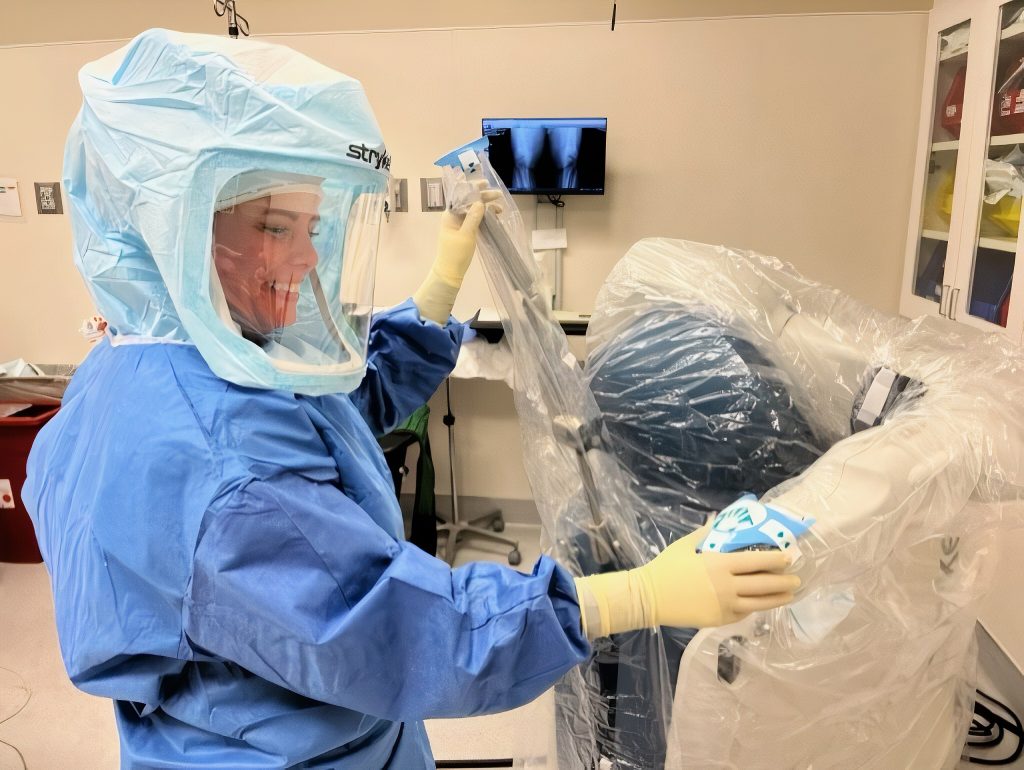 people in blue scrubs and full head masks clean a robotic arm