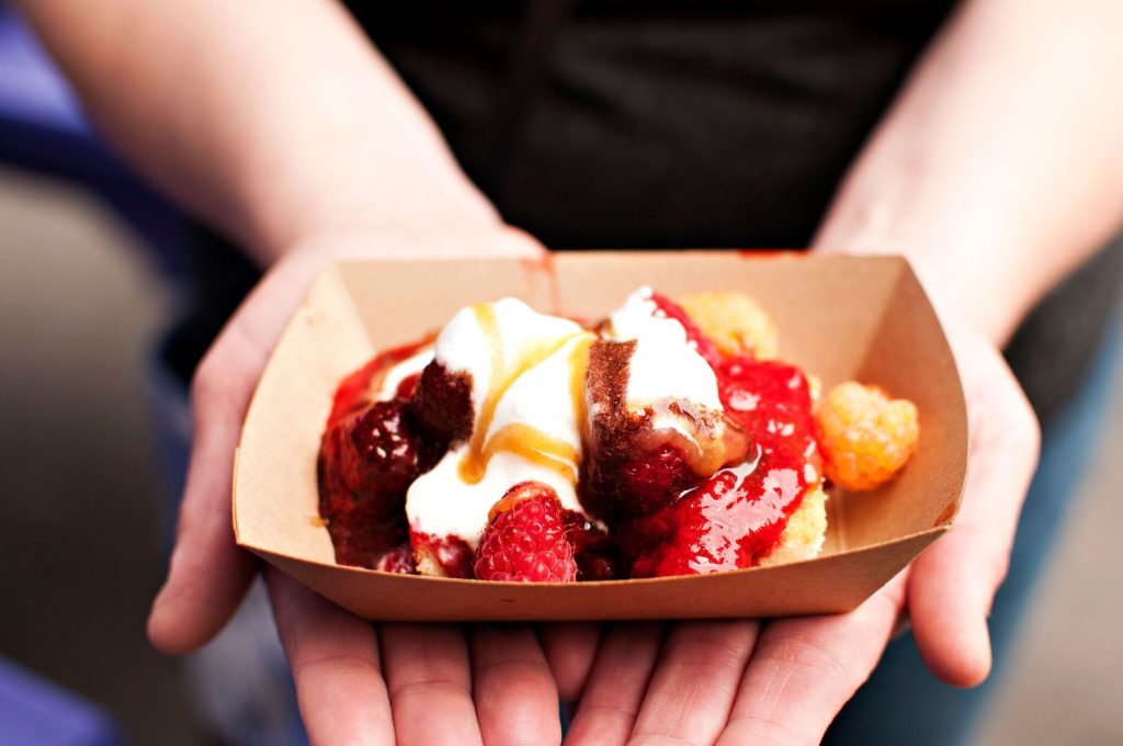 Person holding a cardboard dish of strawberry shortcake in their outstretched hands