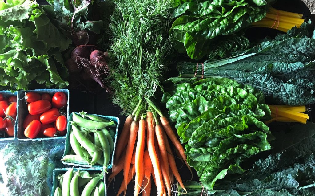 an assortment of summer vegetables including carrots with their green tops, radish and more all together on a display