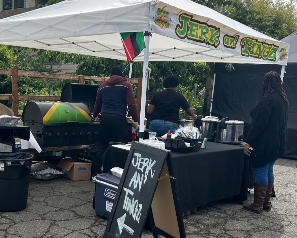Jerk an’ Tingz pop up tent with food on tables, a sign with their name on it and two people serving food