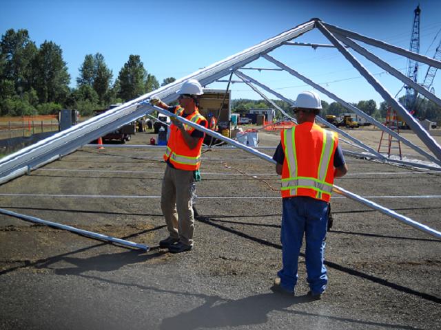 two men in orange construction vests putting up steel tent frame