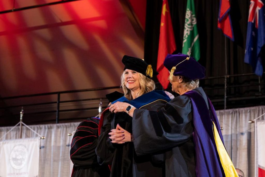 Saint Martin's University in Lacey hooded doctoral graduates hug each other on stage