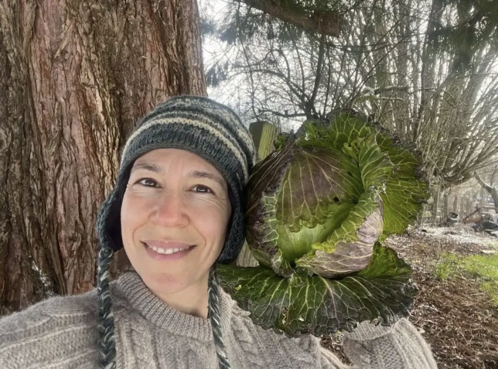 woman holding a cabbage head as big as her head up on her shoulder
