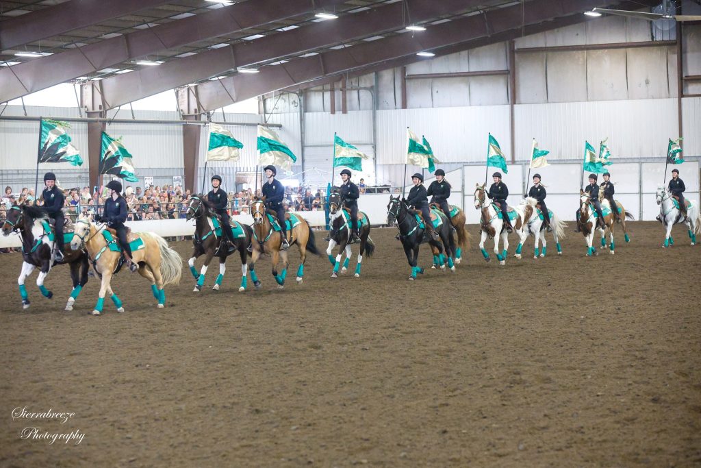 high school equestrian drill riding down the centerline, all carrying green and white flags