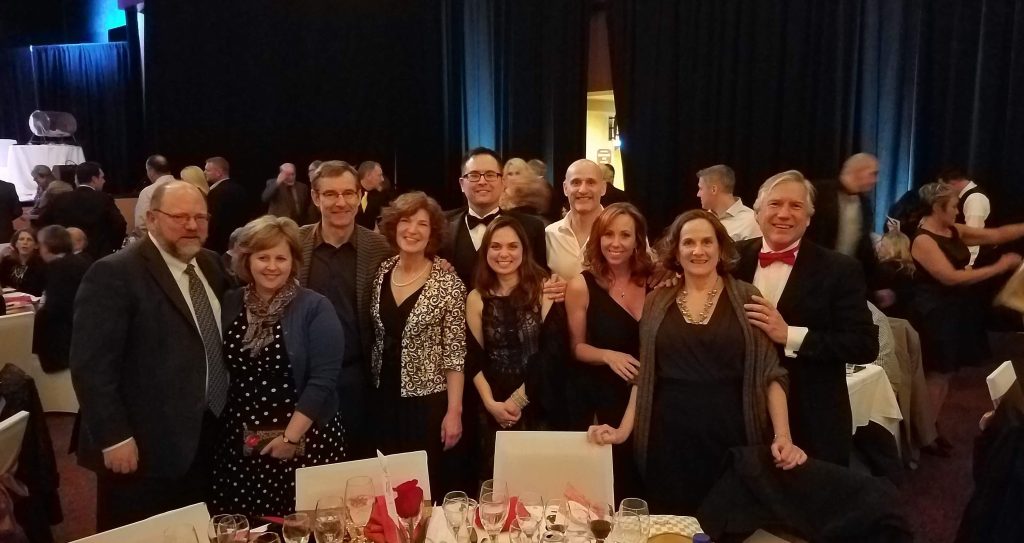 Large group of people dressed up and posing for a photo inside a banquet hall behind a table