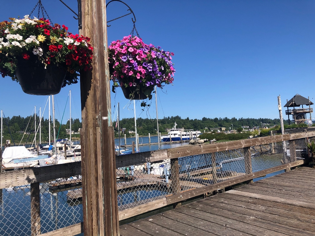 Olympia's Percival Landing Boardwalk with colorful hanging baskets and ships docked in the distrance