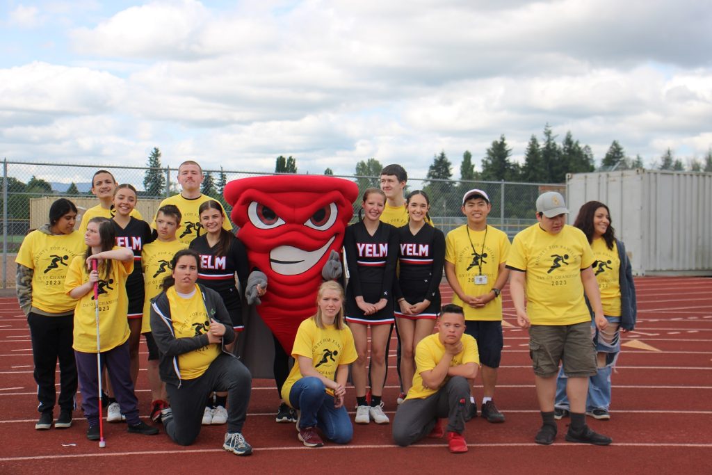 Yelm mascot and cheerleaders posing for a group photos with a bunch of students in yellow shirts
