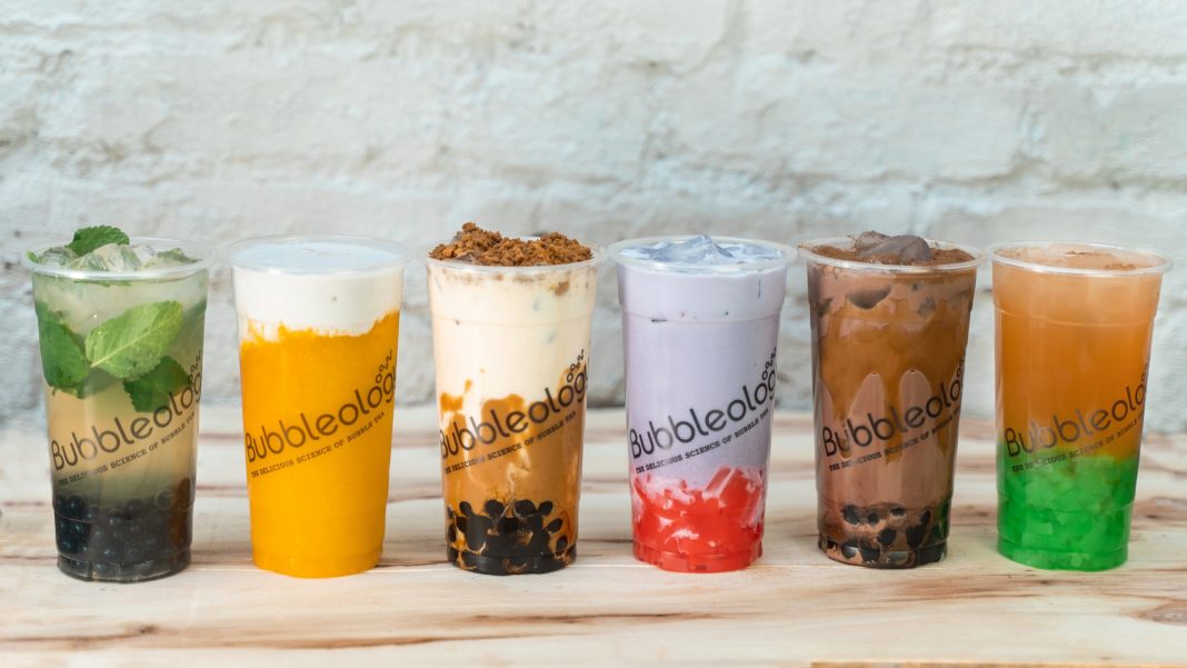 a row of six different bubble tea drinks on a wooden surface with a grey stone background