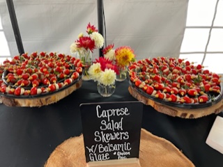 table with a black tablecloth and two large trays of appetizers with a sign that says, 'caprese salad skewers with balsamic glaze. Gluten free.'