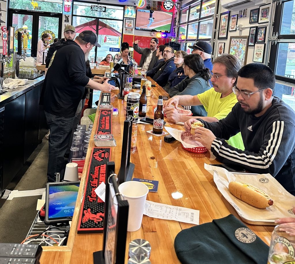 lots of people sitting at a bar easting hot dogs.