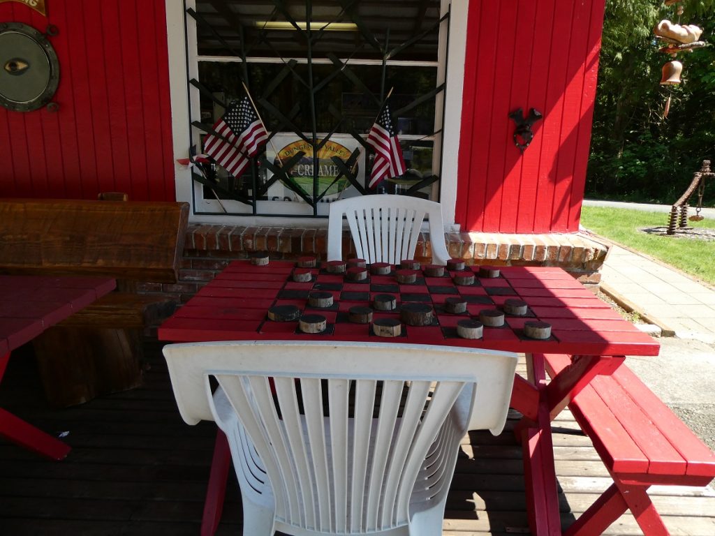 white chairs and a red table with a checker board on it, sitting on a board near a red building