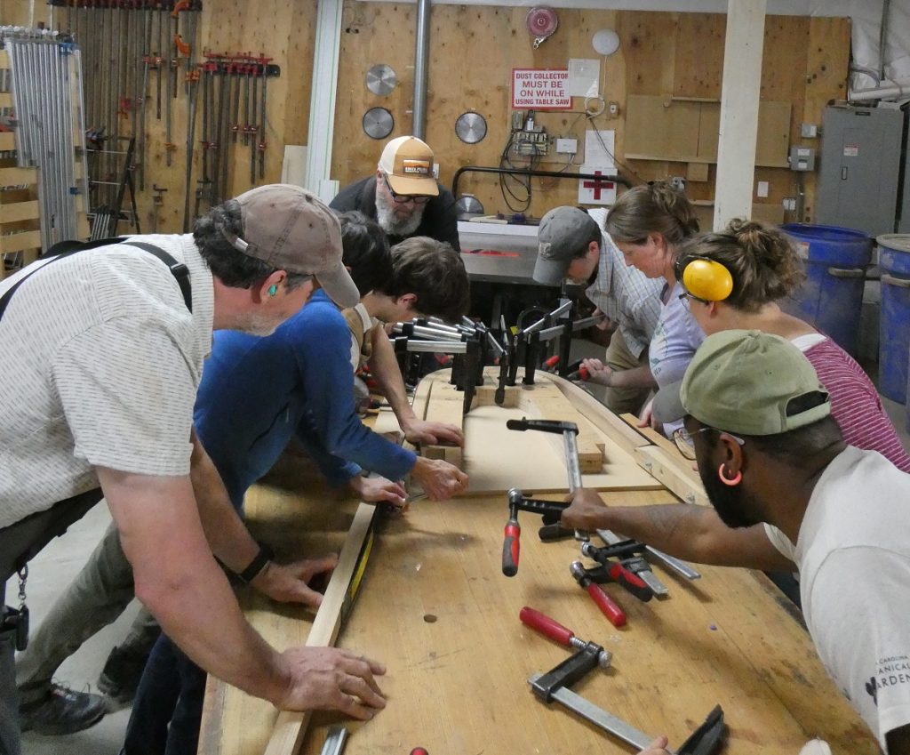 a group of people working on a chair leg on a table with a saw and other tools on it