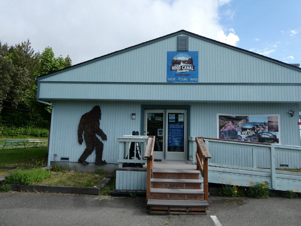 White shop building, with wooden doors leading up to the doors and a metal bigfoot on the side of the building