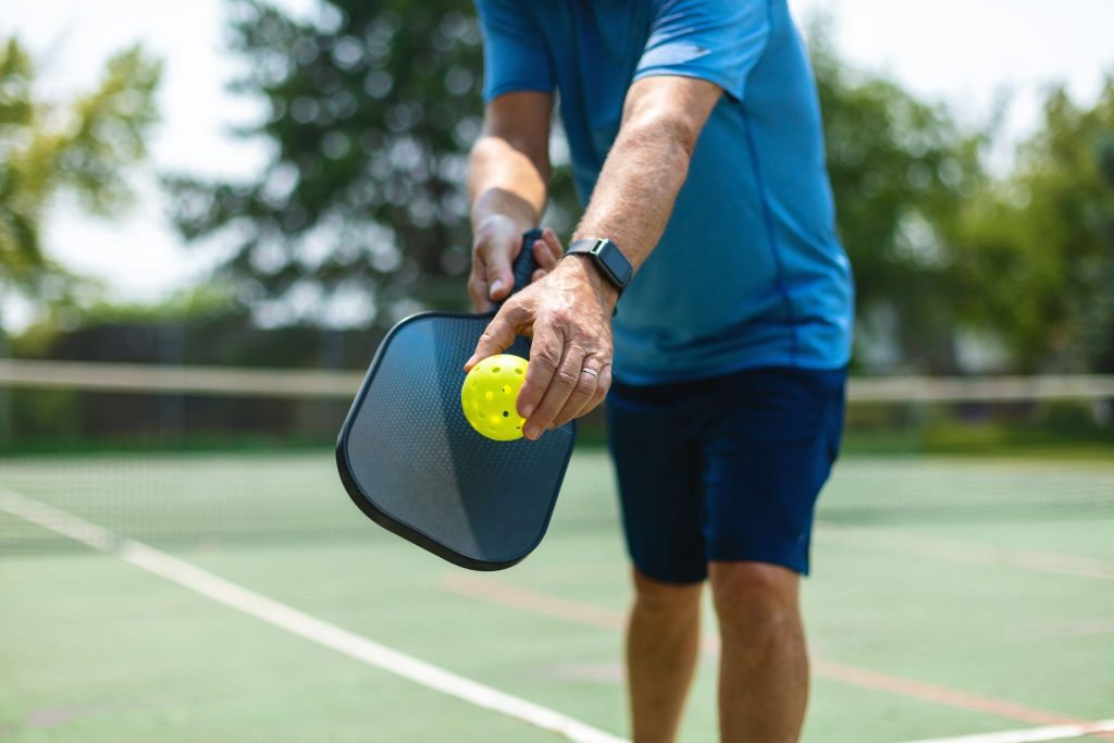 a man on a pickle ball court about to serve, his head is not visible.