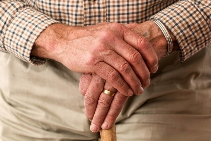 a close up of a man in khakis and a plaid shirt with just his hands showing, one hand is clasping the other