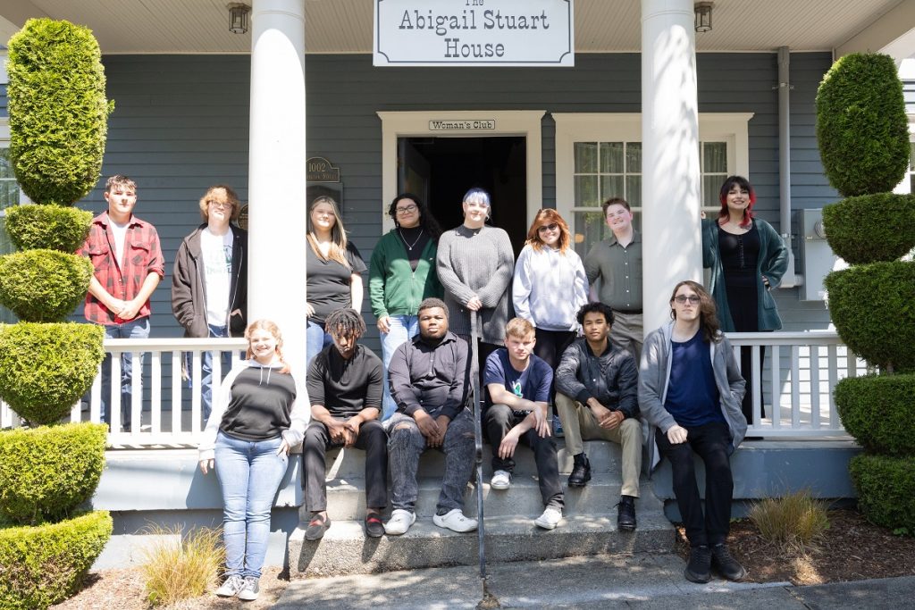 The 2023 All Kids Win Scholarship winners pose on the porch of the Abigail Stuart House, some sitting on the steps. 