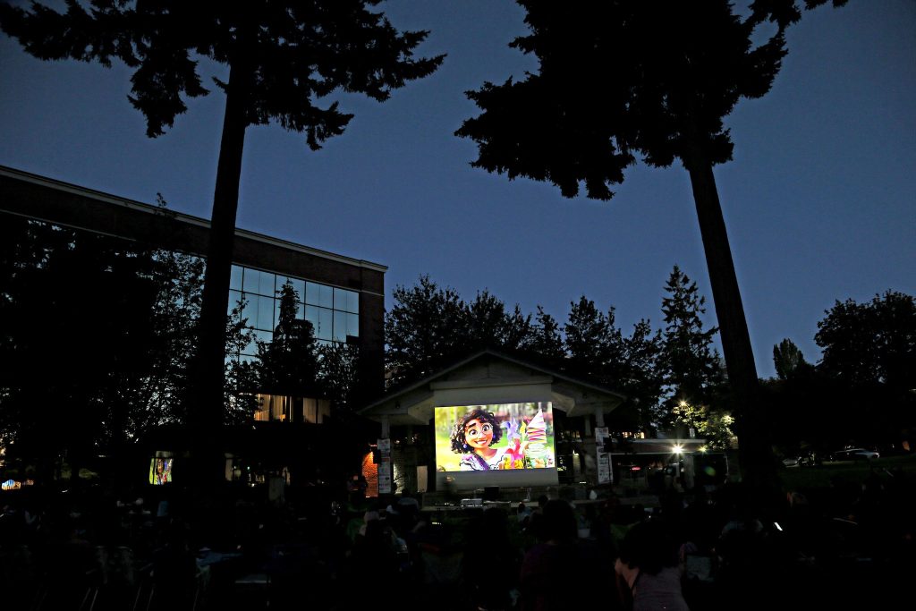 A movie is projecting on a giant screen at night in a park