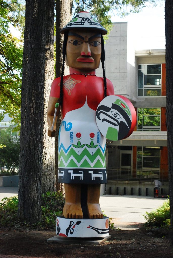 Wooden sculpture of a woman in Native American dress with a drum.