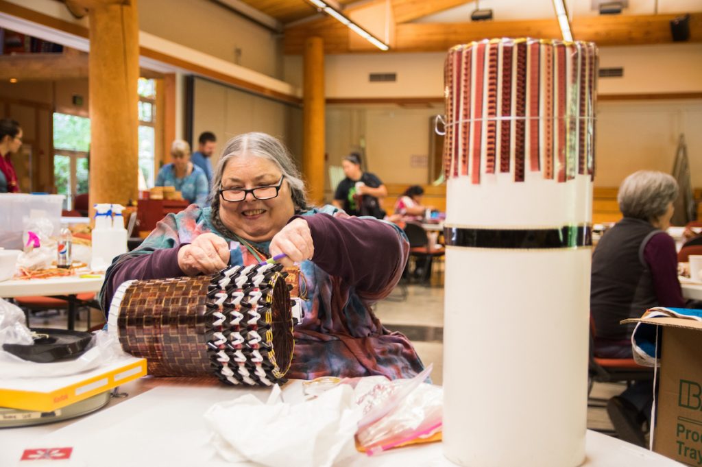 Gail Tremblay sitting at a table in the Evergreen Longhouse weaving a basket