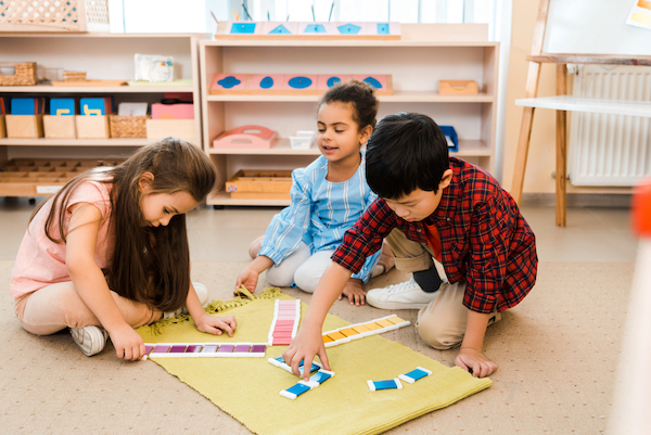 a boy and two girls play on a mad with colored tiles in a classroom
