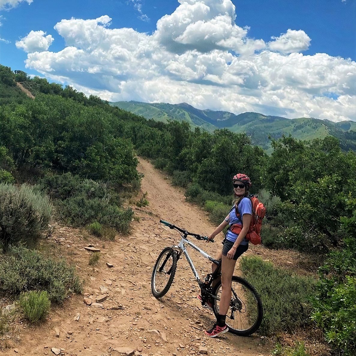 Dr. Kaley Capitano standing next to a bike on a dirt trail surrounded by brush