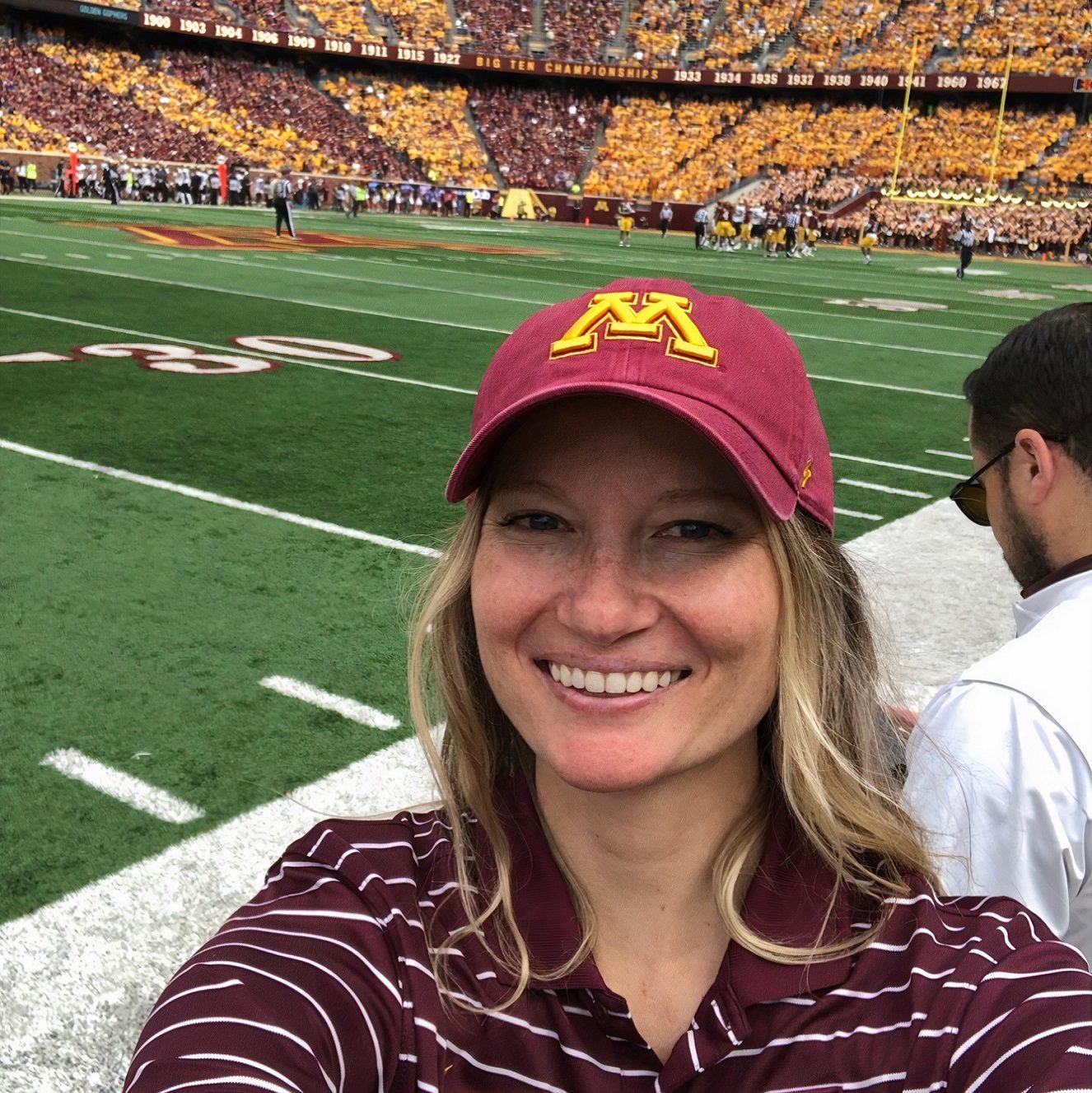 Dr. Kaley Capitano smiling for a selfie at a football stadium, the field is in the background.
