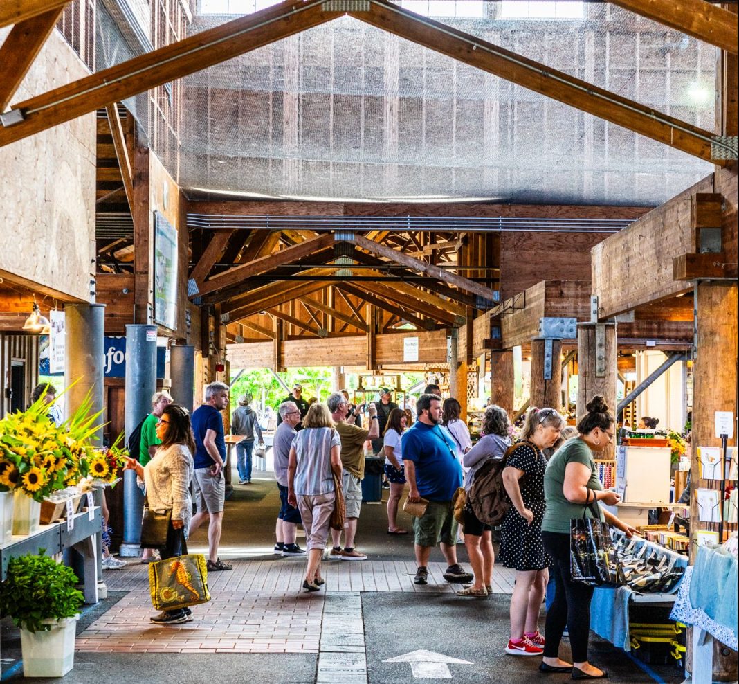 People milling around under the Roof of the open-air Olympia Farmers Market