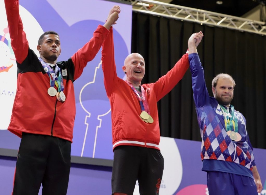 Mitch Hibdon and two other people stand on podium, holding hands while raising arms above their heads