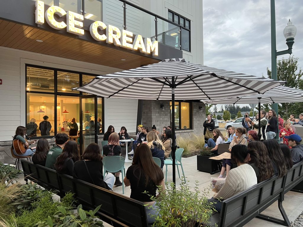 A building with the words, 'Ice cream' on it with a patio full of people and a table with an umbrella