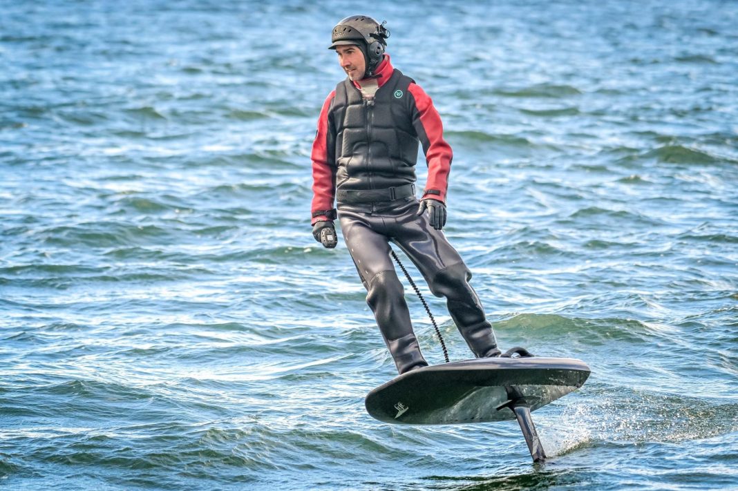 a man on an eFoil wearing a helment and a wetsuit.