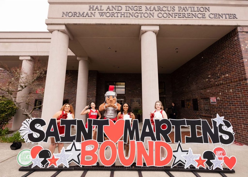 Four Saint Martin's University cheerleaders and the mascot pose behind a sing that says, 'Saint Martin's Bound' with stars on it