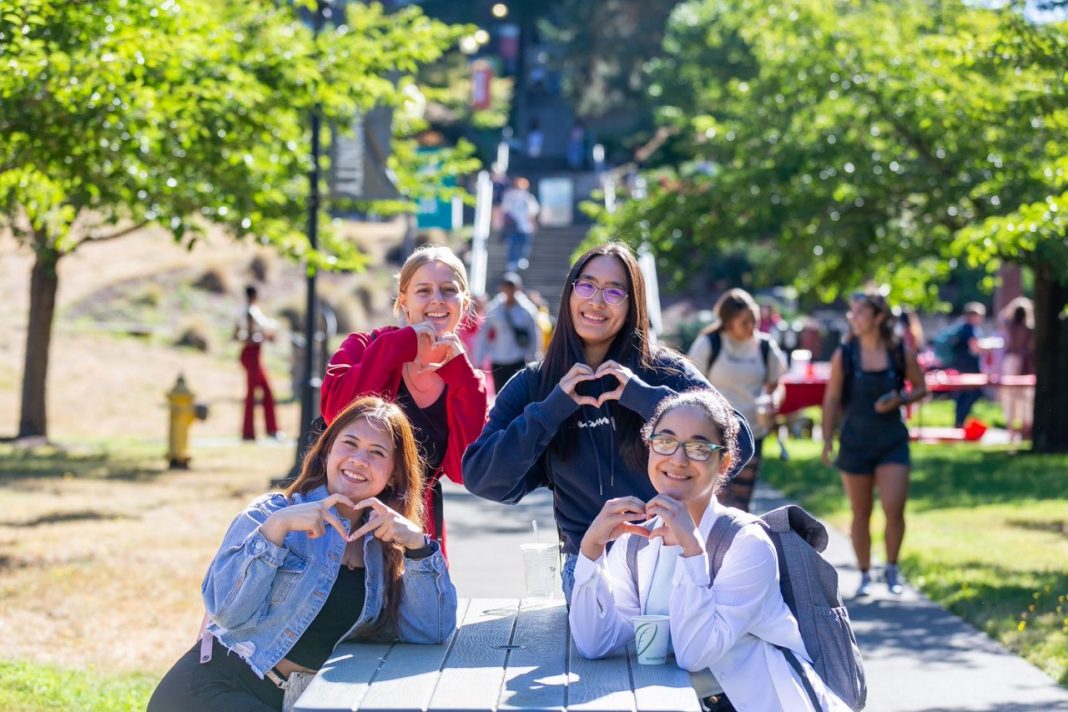 four young girls lean over a concrete rectangle, smiling and forming hearts with their hands