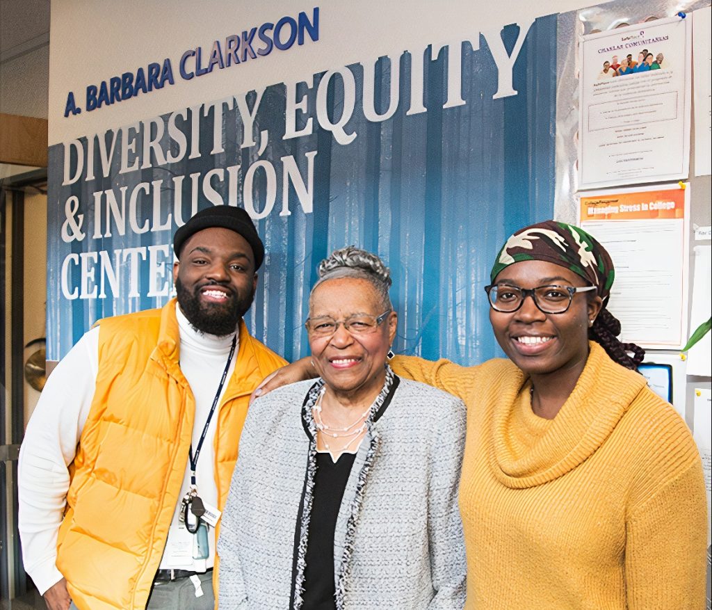A Black man and two Black women pose for a photo by the wall that reads, 'A. Barbara Clarkson, Diversity, Equity, & Inclusion Center.'