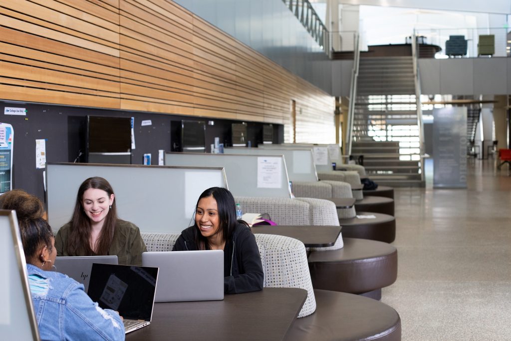three female college students sit at a table with laptops