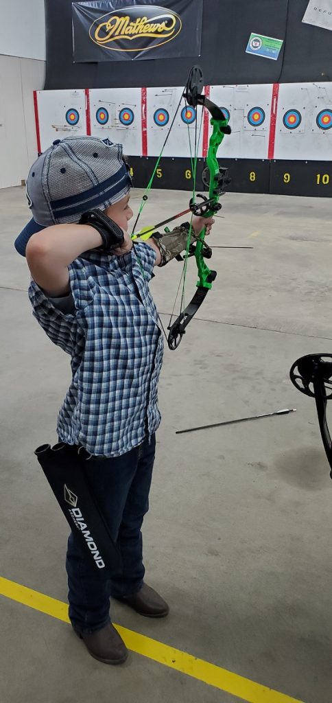 A boy draw back his compound bow in an indoor shooting range