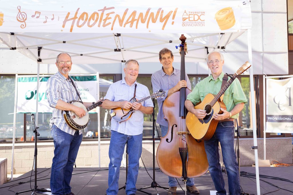 four men one holding a banjo, one a violin, one a bass and one a guitar stand on a stage with a banner that says, 'Hootenany!'