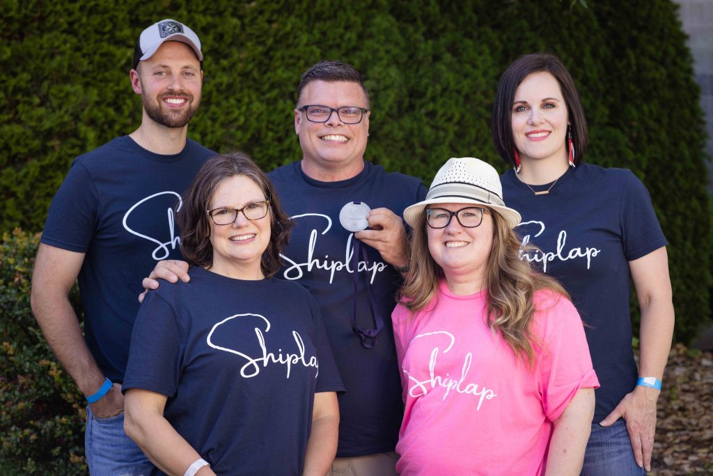 four people in blue shirts and one in a pink shirt pose for a group photo