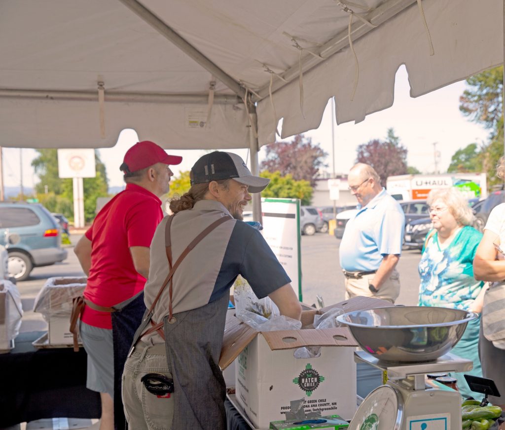 Two workers in a white tent smile at customers as they take chilis out of cardboard boxes